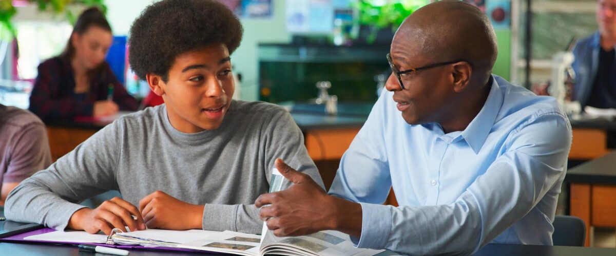 Male High School Student Receiving Individual Attention From Teacher In Science Class